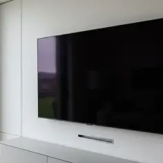 Nowoczesny telewizor na ścianie, idealne rozwiązanie jak ukryć kable. Minimalistyczna zabudowa i ukryte przejścia kablowe.