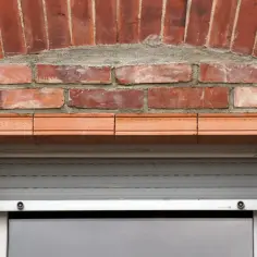 Ceglany łuk nad oknem, z ozdobnym nadprożem i roletą.