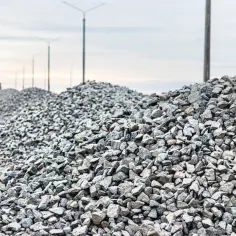 Duże hałdy kruszywa do betonu czekają na budowie. W tle widać latarnie i maszynę budowlaną.
