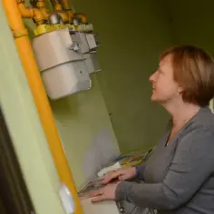 Kobieta patrzy na liczniki gazowe zamontowane na żółtej rurze.
