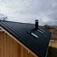 Czarny, metalowy dach domu z lukarnami i kominem, widok z góry.