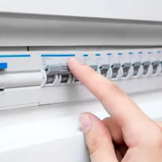 Palec naciska wyłącznik w skrzynce elektrycznej. Zastanawiasz się, ile kosztuje postawienie skrzynki elektrycznej na działce?