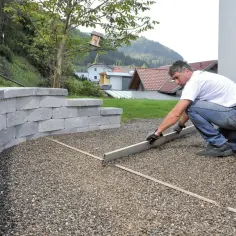 Mężczyzna przygotowuje teren pod budowę podjazdu do garażu z betonu, wyrównując podłoże z kruszywa.