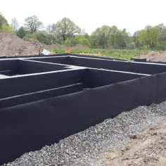 Izolacja starych fundamentów z kamienia, zabezpieczona czarną membraną i otoczona żwirem. Budowa w toku.