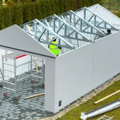 Budowa garażu blaszanego w toku. Pracownicy montują konstrukcję dachu. Czy garaż blaszany wymaga pozwolenia?
