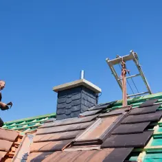 Budowlaniec na dachu układa dachówki. Zastanawiasz się, czym ocieplić komin na strychu?