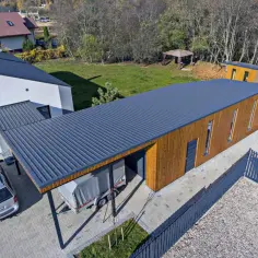 Nowoczesny garaż z drewnianą elewacją i dachem z blachy trapezowej. Obok stoi przyczepa.