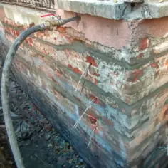 Naprawa ścian nośnych z widocznymi pionowymi pęknięciami. Widać wstrzykiwany materiał i kotwy.