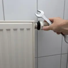 Ręka z kluczem przy termostacie grzejnika. Możliwa wymiana grzejnika w bloku bez spuszczania wody.