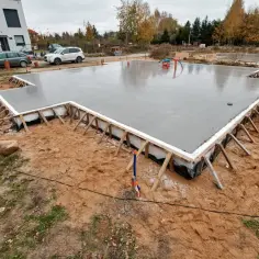 Świeżo wylana płyta fundamentowa, gotowa na budowę domu. Widać zbrojenie i szalunki.