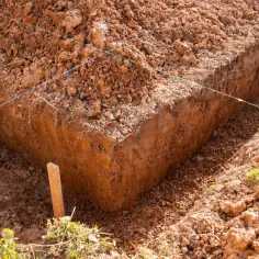 Wykonano wykop pod ławy fundamentowe. Widać ziemię, sznurki wyznaczające linie i drewniany palik.
