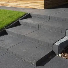 Schody z bloczków betonowych, pokazujące, jak wymurować schody z bloczków betonowych. Obok trawnik i drewniana elewacja.