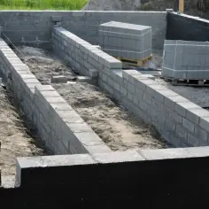 Budowa fundamentów: betonowe pustaki czekają na izolację ścian fundamentowych. Piasek i sznurki wyznaczają linie budowy.