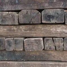 Stare, drewniane podkłady kolejowe w ogrodzie, tworzące rustykalną ścianę. Widać metalowe zaczepy.