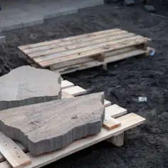 Płaskie kamienie na ścieżkę leżą na drewnianych paletach, gotowe do ułożenia.