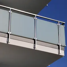 Nowoczesne mocowanie balustrady od czoła z matowego szkła i stali nierdzewnej na tle błękitnego nieba.