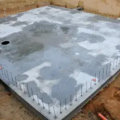 Gotowy dom na płycie fundamentowej, zbrojenie wystaje z betonu, czekając na kolejne etapy budowy.
