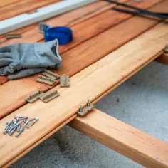 Budowa tarasu z bloczka betonowego w toku. Widać wkrętarkę, rękawice, wkręty i elementy montażowe.