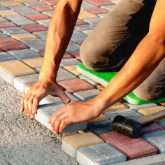 Ręczne układanie kostki brukowej na betonie. Kolorowe kostki tworzą wzór, a pracownik precyzyjnie dopasowuje kolejny element.