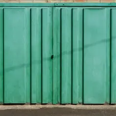 Zielona, dwuskrzydłowa brama garażowa z przetłoczeniami, osadzona w ceglanej ścianie. Projekt bramy garażowej dwuskrzydłowej.