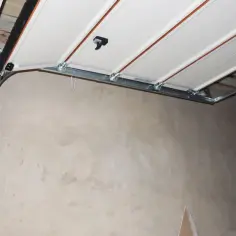 Mechanizm bramy garażowej uchylnej w trakcie montażu. Widoczne prowadnice, zawiasy i panel bramy.