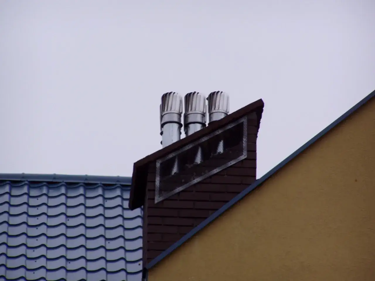 Trzy metalowe nasady kominowe na ceglanym kominie wentylacyjnym, zapewniające prawidłowe zakończenie komina wentylacyjnego.