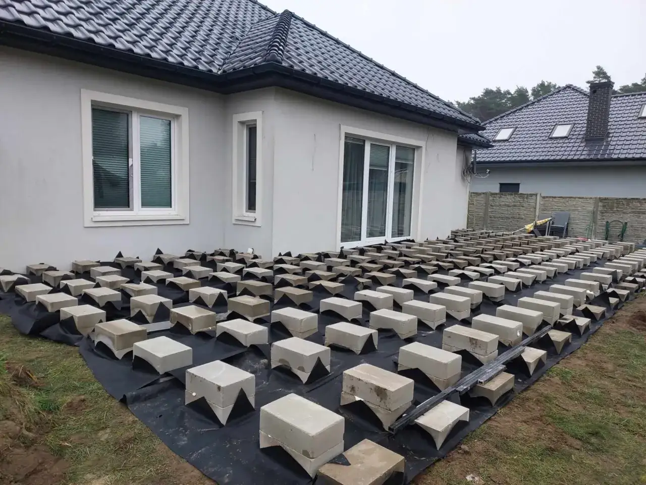 Budowa tarasu z bloczka betonowego. Podkład z czarnej agrowłókniny, na nim ułożone bloczki tworzące ruszt pod przyszłą nawierzchnię.
