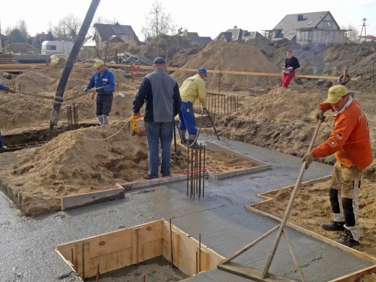 Pracownicy wykonują odkopanie i izolację fundamentów, wylewając beton na budowie.