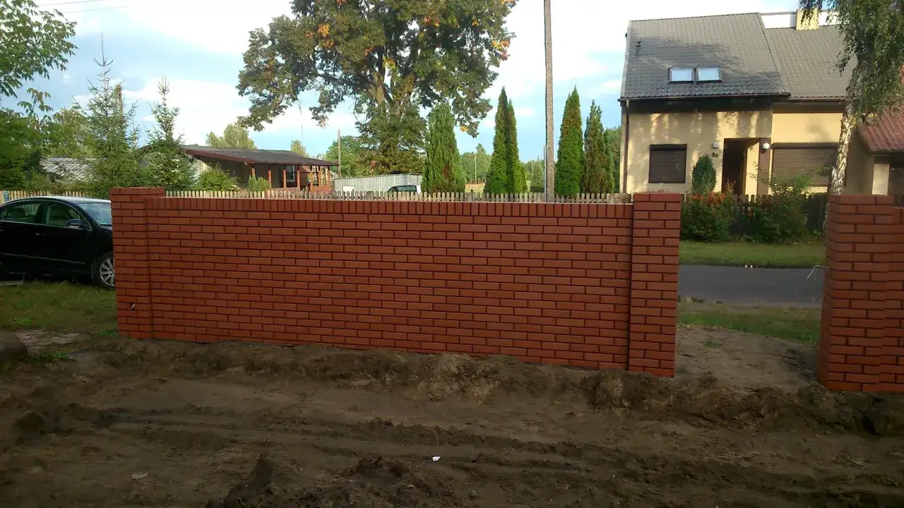 Solid brick fence, recently built, with a wooden picket fence on top. A black car is parked to the left.