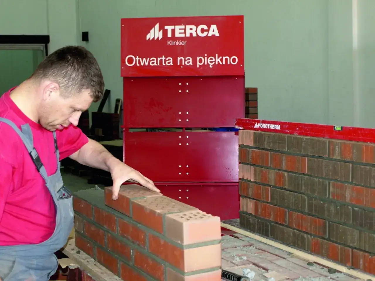 Budowniczy układa cegły, wykonując murowanie ścianek działowych. Poziomica Porotherm wskazuje precyzję pracy.