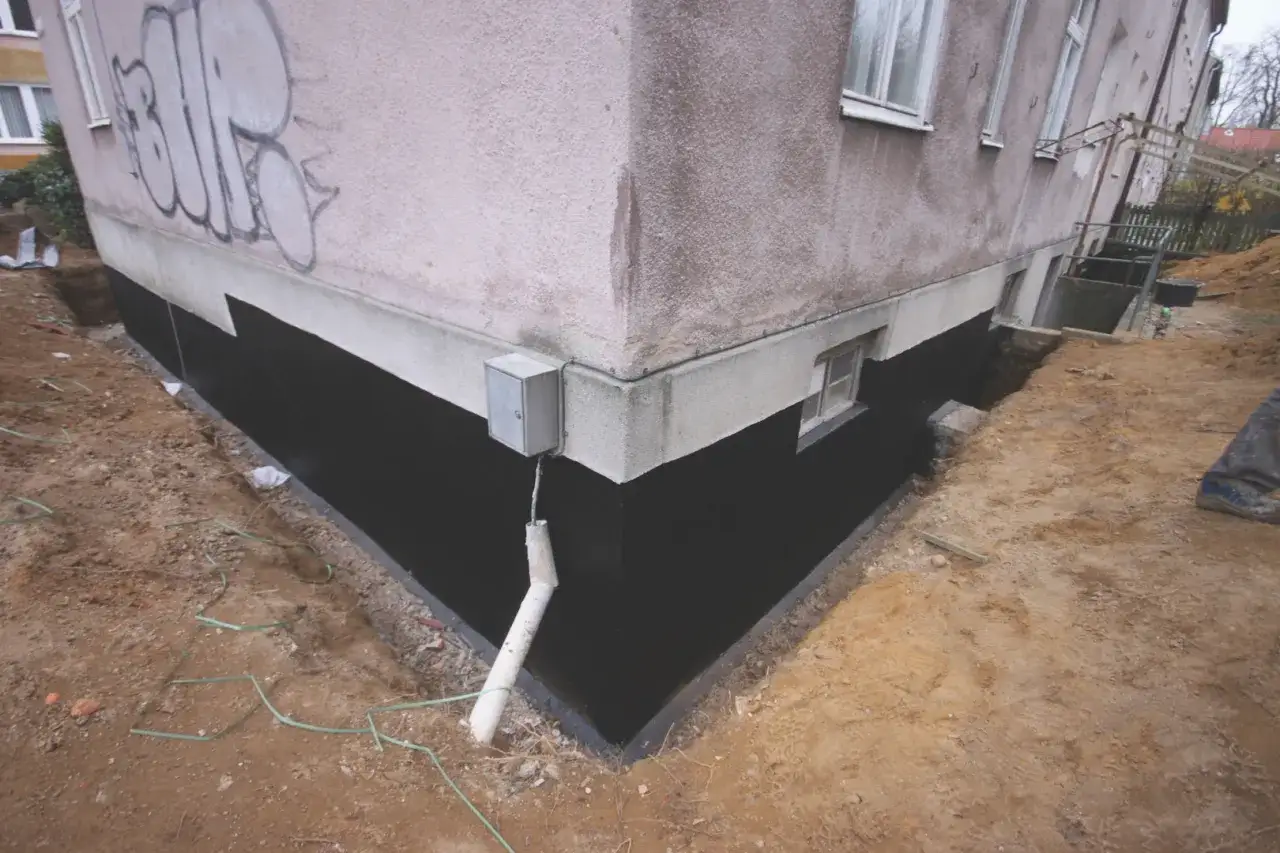 Prace przy starym domu: jak ocieplić fundamenty, izolacja czarną masą, wykopane ziemia, rynna odprowadzająca wodę.