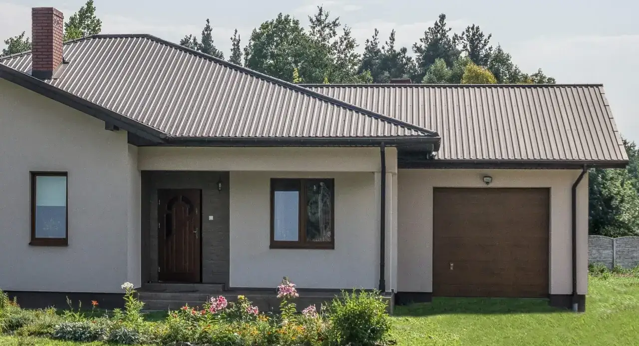 Nowy dom z brązową matową blachą trapezową na dachu i bramą garażową.