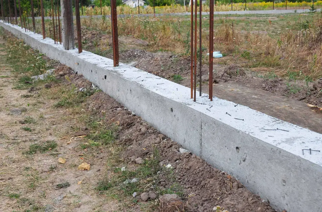 Solidny murek pod ogrodzenie, z wystającymi prętami zbrojeniowymi, czeka na dalsze prace budowlane.