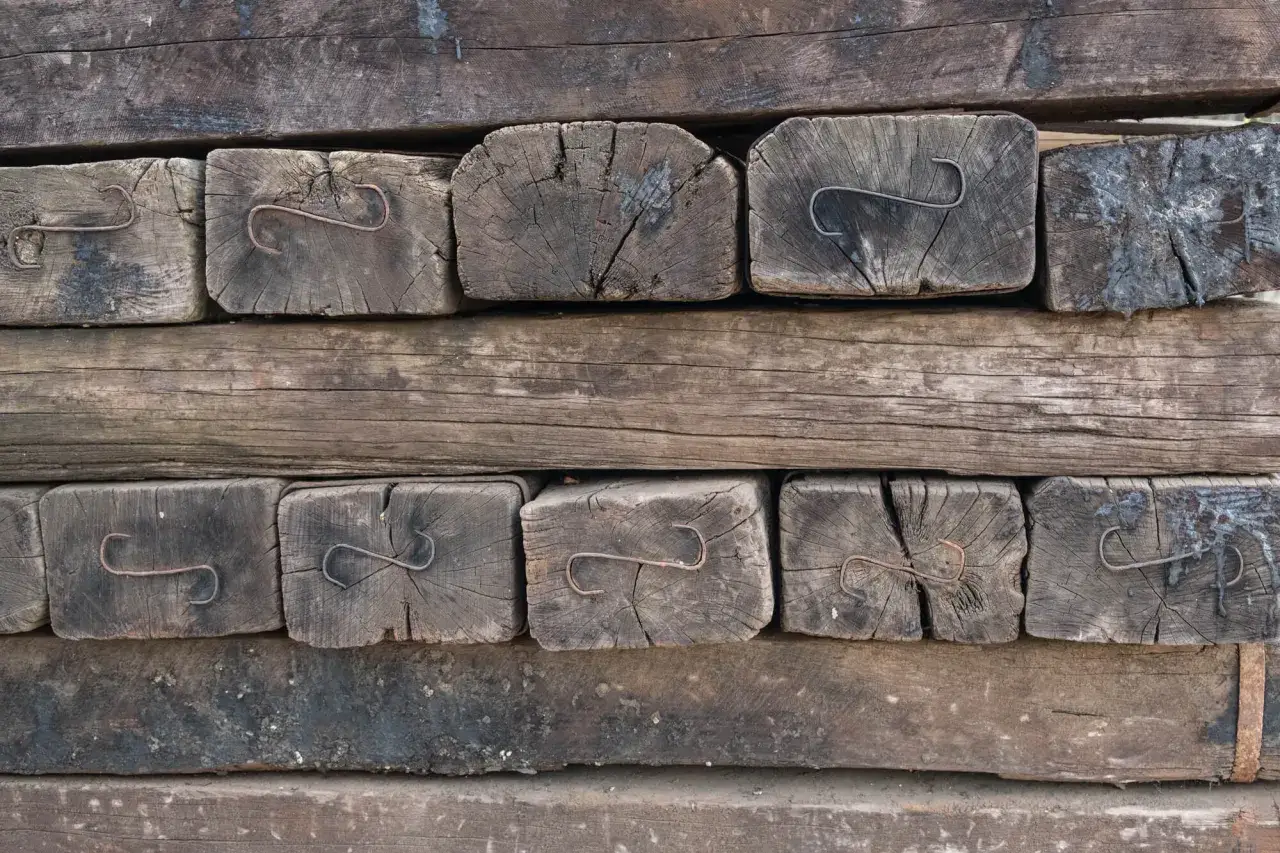 Stare, drewniane podkłady kolejowe w ogrodzie, z widocznymi metalowymi elementami.