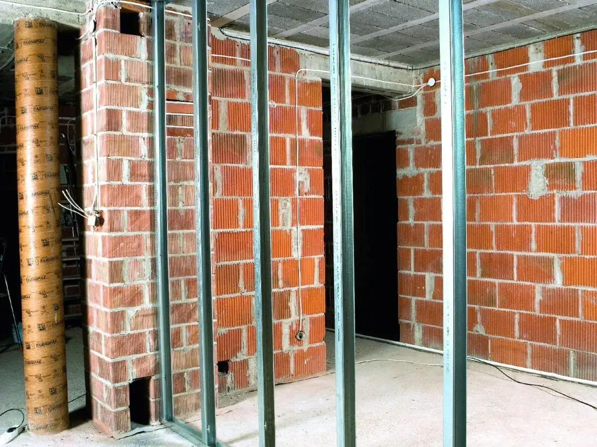 Trwają prace nad murowaniem ścianek działowych. Widać ceglane ściany i metalowe profile konstrukcyjne.