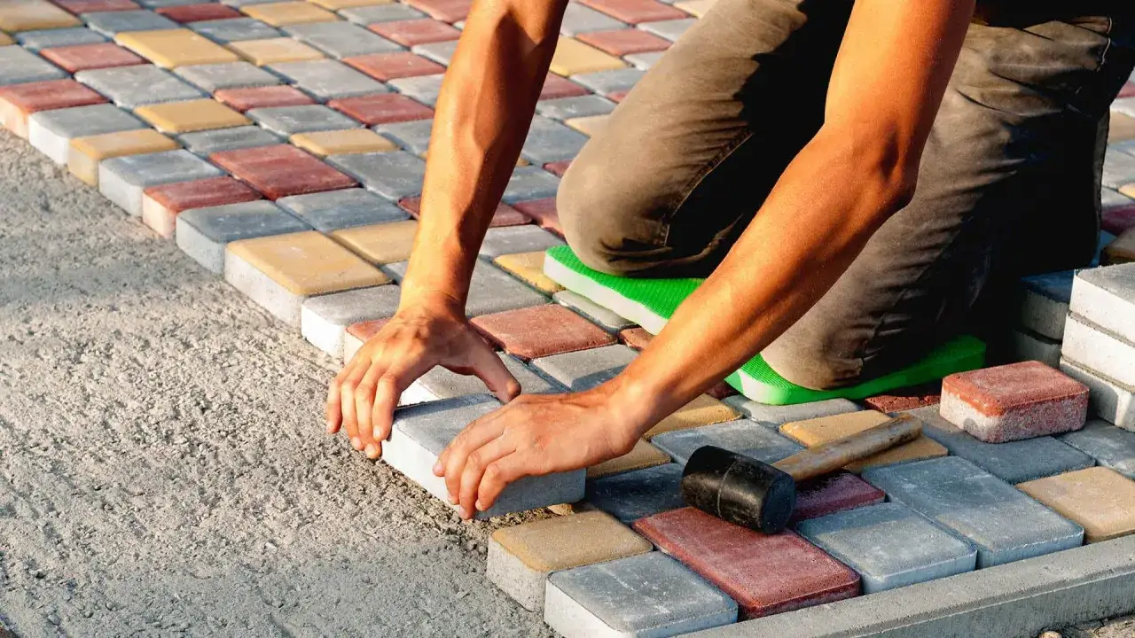 Ręczne układanie kostki brukowej na betonie. Kolorowe kostki tworzą wzór, a pracownik precyzyjnie dopasowuje kolejny element.