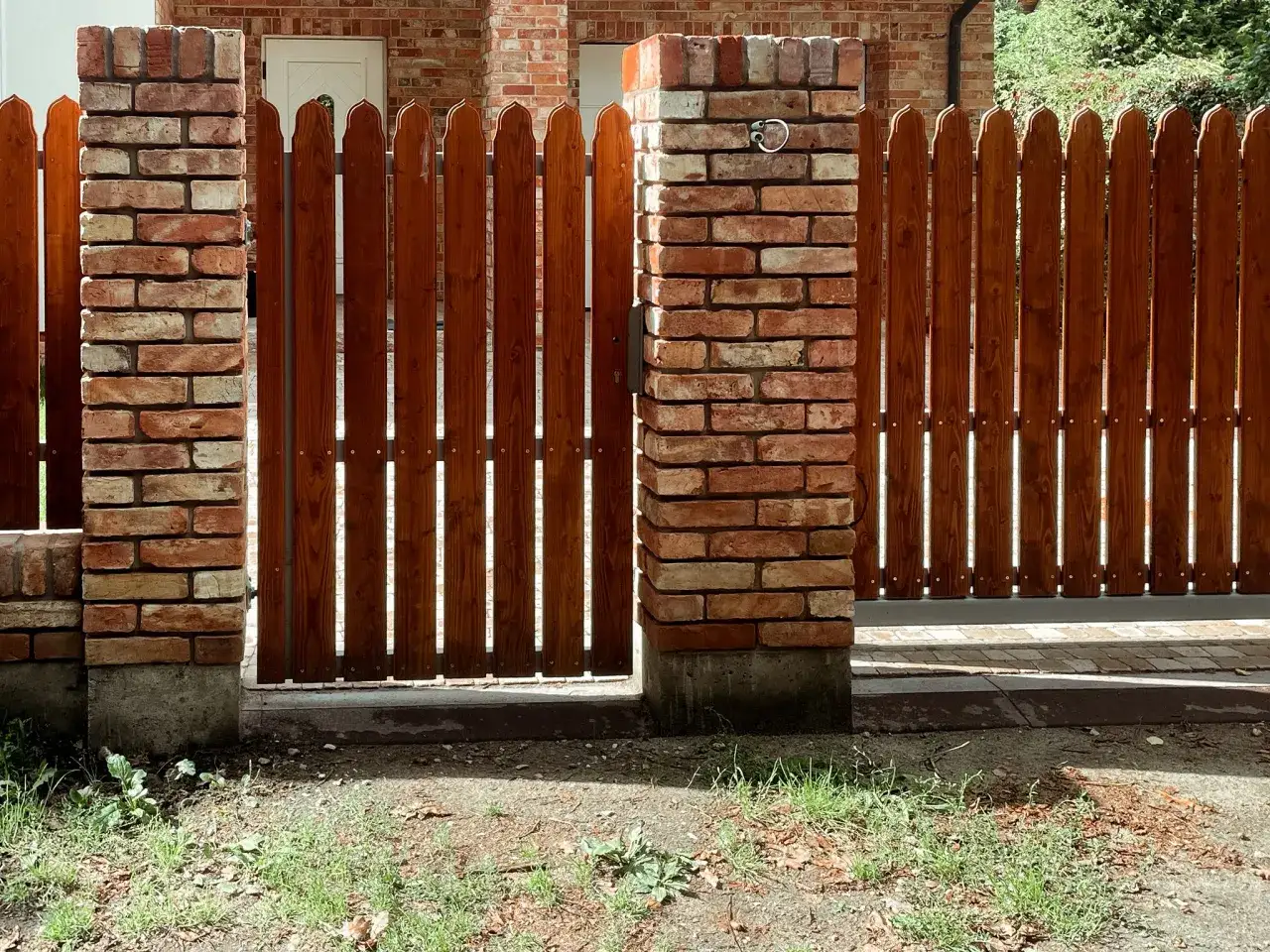 Solidne ogrodzenie ze starej cegły i drewna, z ozdobnymi słupkami i drewnianą bramą.