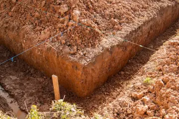 Wykonano wykop pod ławy fundamentowe. Widać ziemię, sznurki wyznaczające linie i drewniany palik.